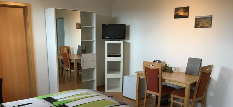 Hotelzimmer mit Bett, weissem Regal, Fernseher und einem Tisch mit zwei Stühlen