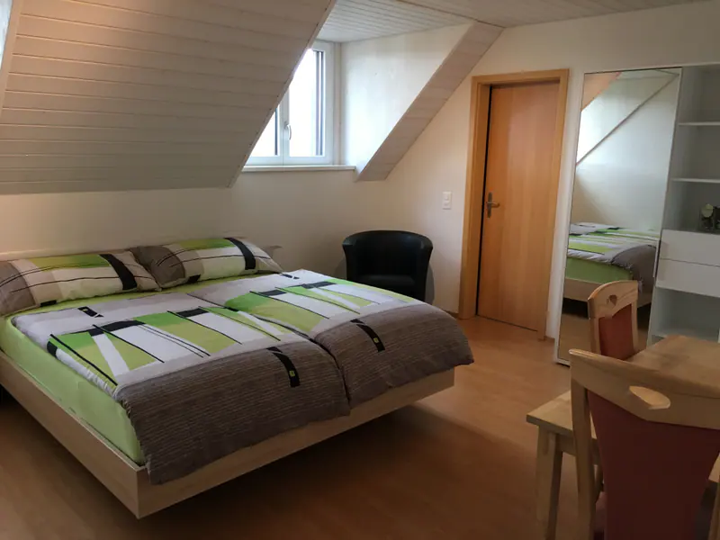 Hotelzimmer unter dem Dach mit Doppelbett, Sessel, Dachfenster und Holztüre