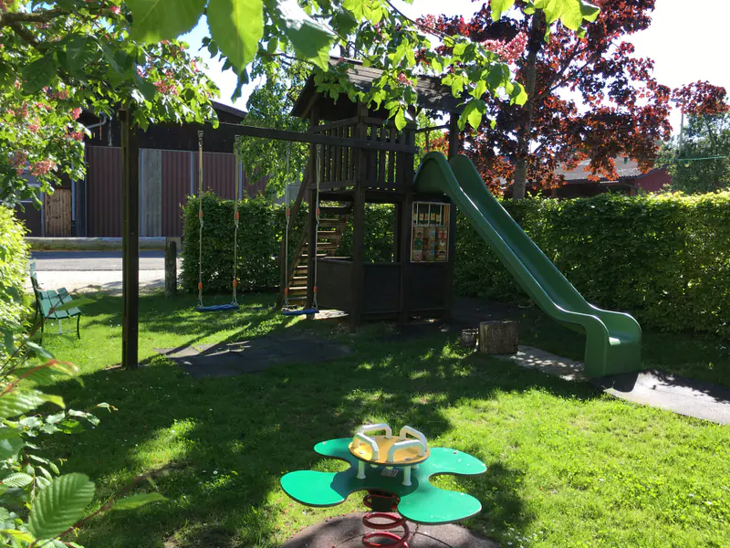 Kinderspielplatz im Garten mit Spielhaus aus Holz, grüner Rutsche, Schaukel und einer Federwippe auf der Wiese