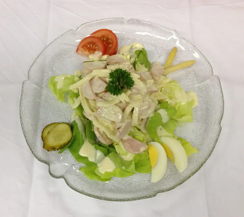 Wurst-Käsesalat mit Ei, Tomate und Essiggurke auf einem Glasteller