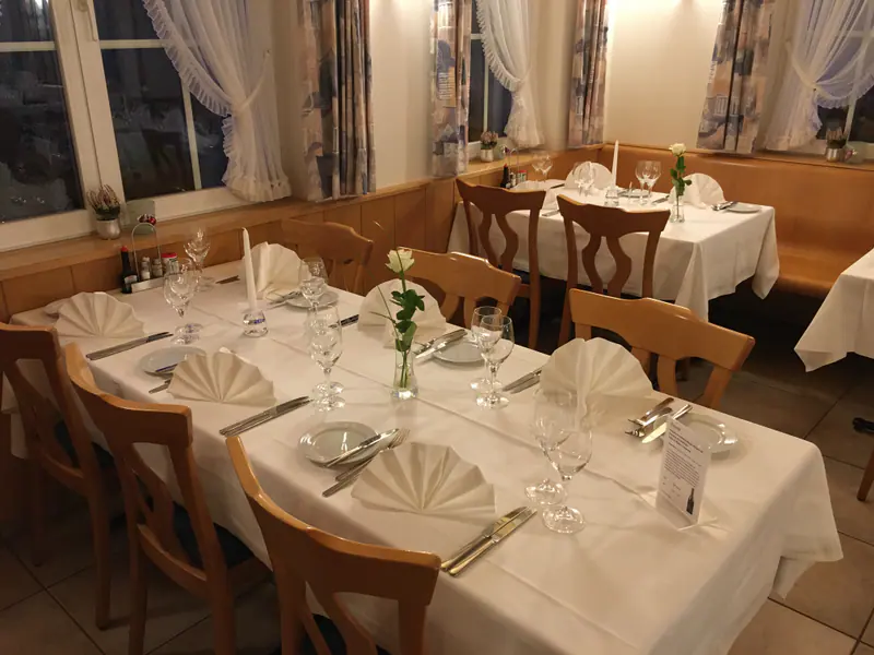 Lange gedeckte Tafel mit weissen Servietten und Holzstühlen, im Hintergrund die Eckbank