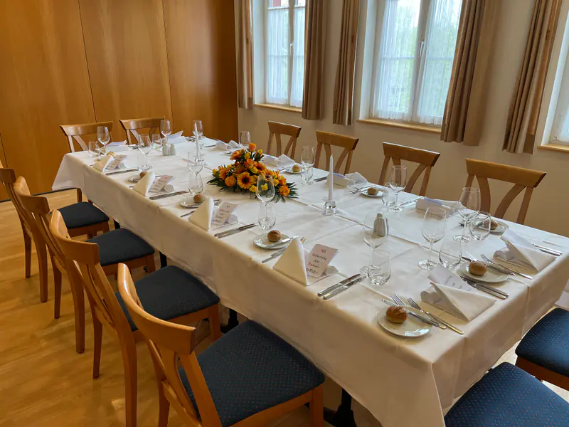 Saal 1 mit langer, weiss gedeckter Tafel, Blumenschmuck und Holzstühlen mit blauen Polstern