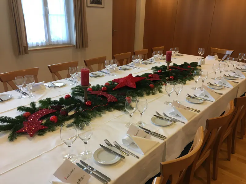 Weihnachtlich geschmückte Tafel im Saal 2 mit Tannenzweigen, roten Sternen und Kerzen
