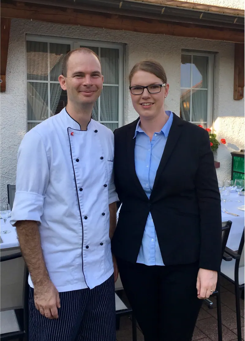 Stefanie und Richard Bürgin nebeneinander vor dem Restaurant; eine Person trägt eine weisse Kochjacke, die andere einen dunklen Blazer